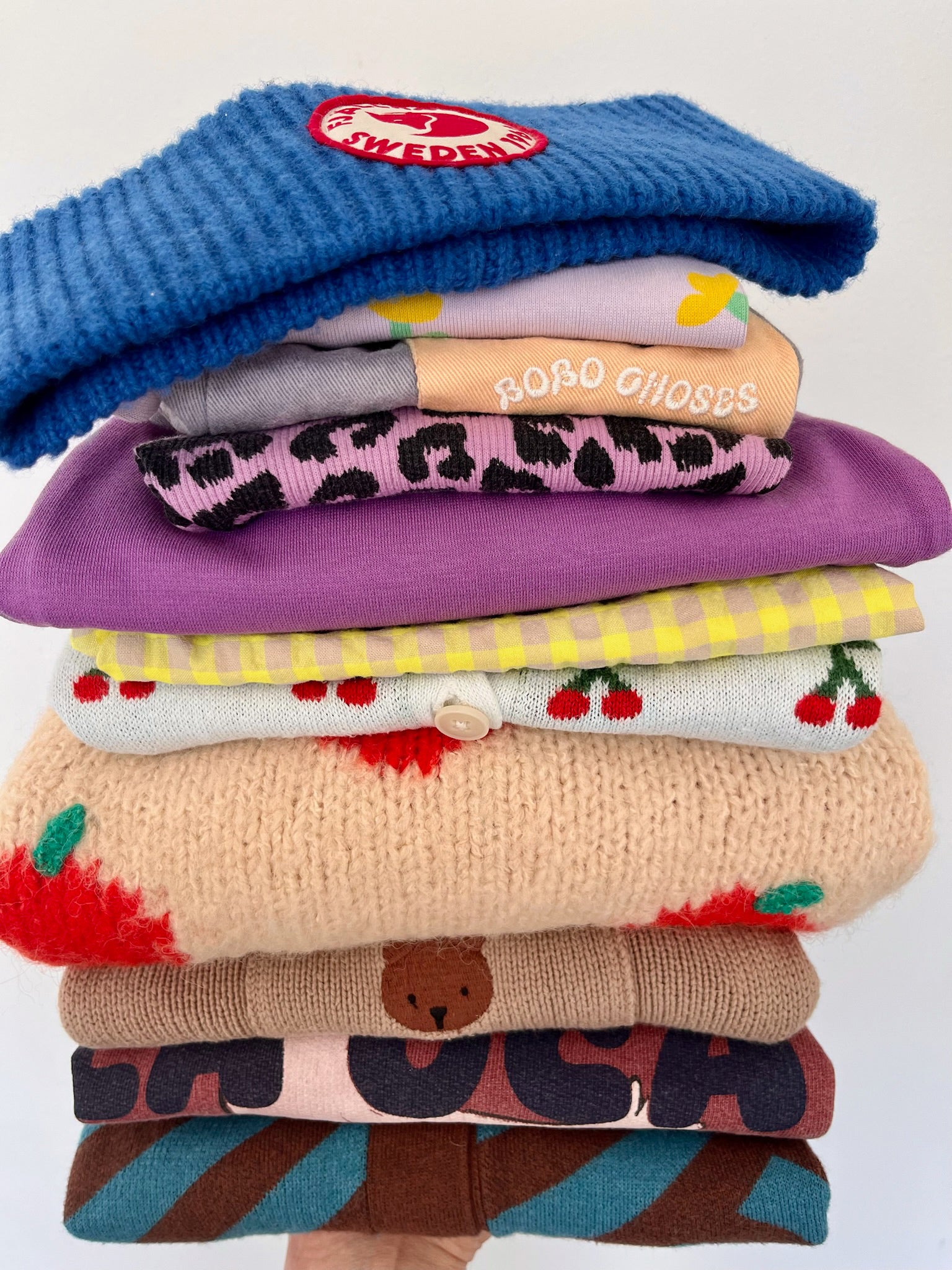 Stack of colorful children's sweaters with visible brand logos on a white background