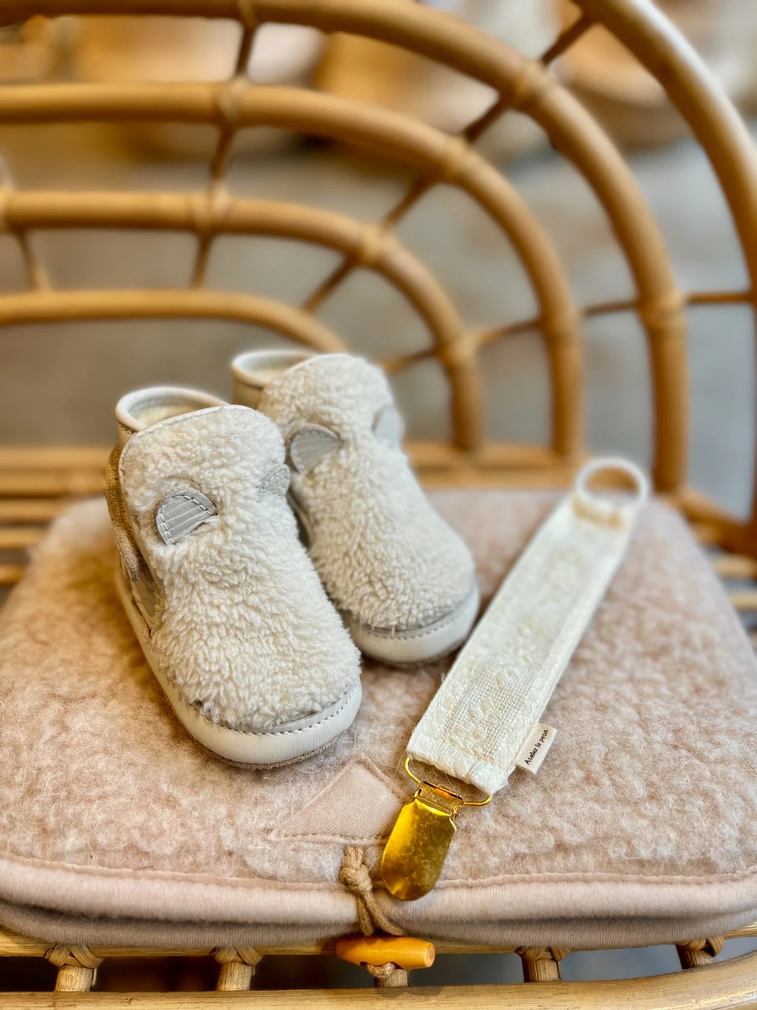 Pair of beige baby shoes on a cushioned chair with a gold strap.